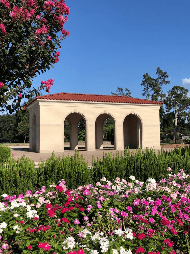 Peaceful gazebo in a scenic outdoor park with vibrant pink and white flowers.
