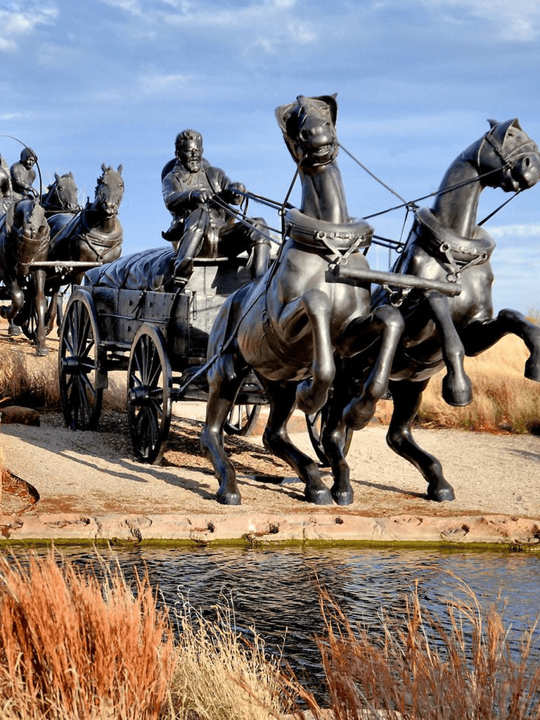 Bronze statue of a historic wagon train with horses and pioneers, outdoor sculpture in a scenic landscape.
