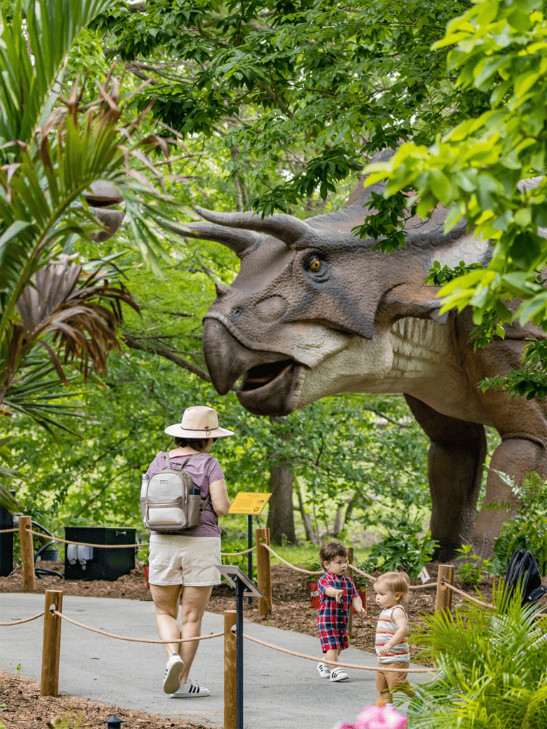 Majestic dinosaur exhibit at Quest for Directions with young visitors exploring nature-themed attractions and educational displays.