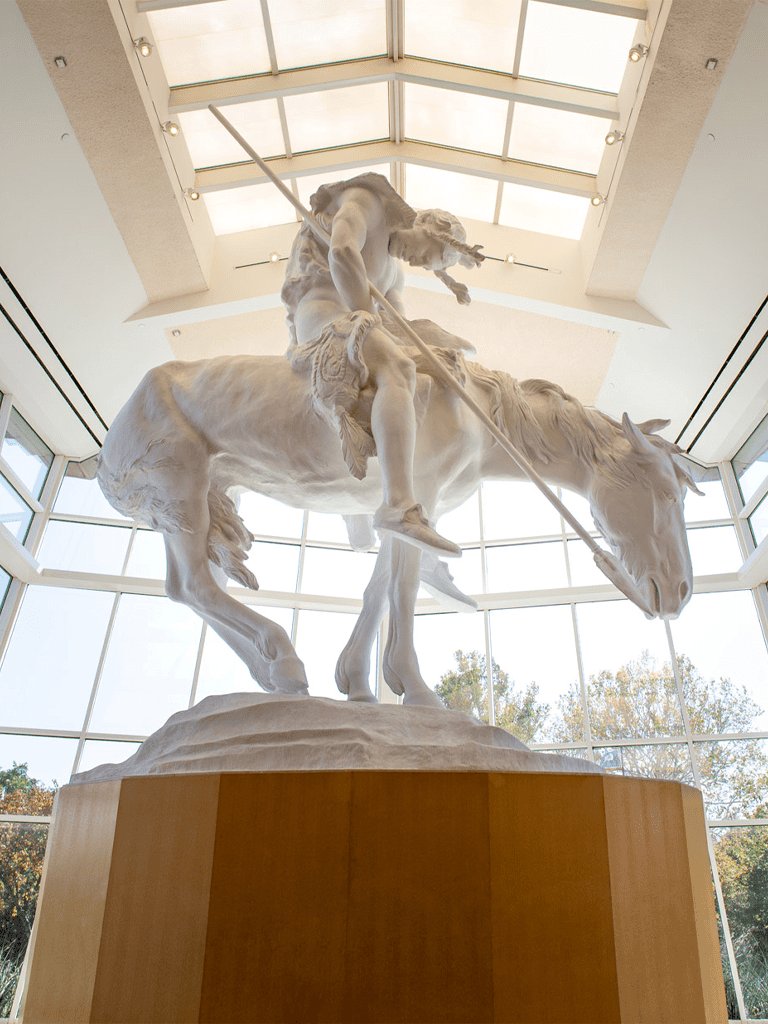 Majestic marble statue of a warrior on horseback in museum interior, glass ceiling sunlight.