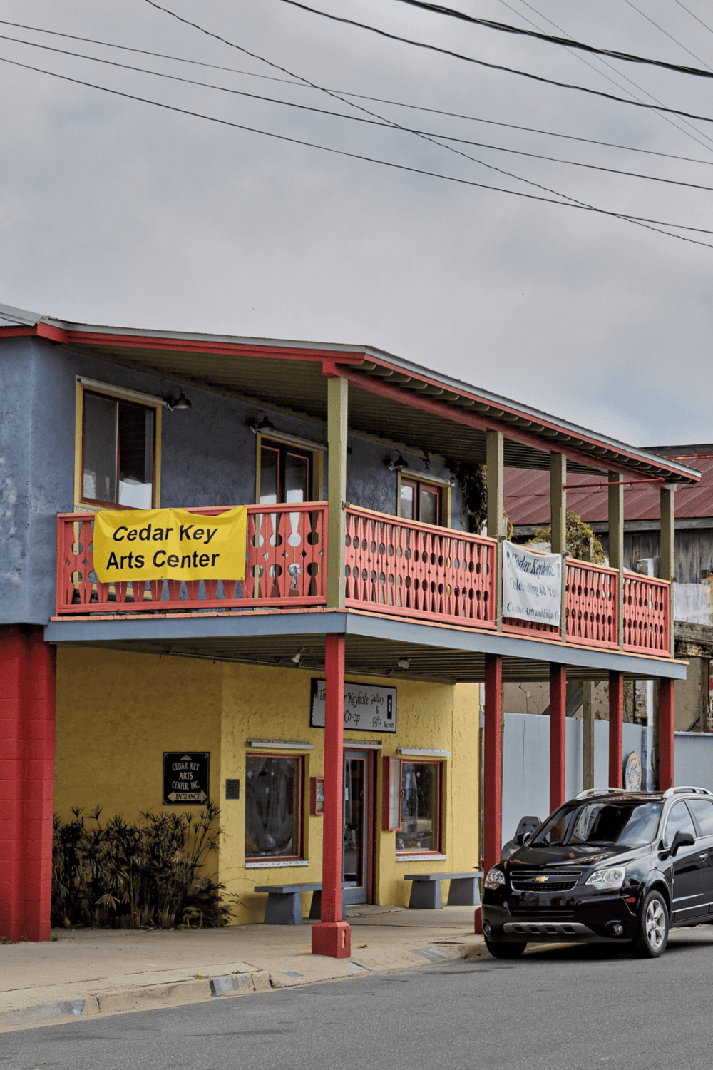 Cedar Key Arts Center building with vibrant yellow and red exterior, featuring signage and outdoor seating.