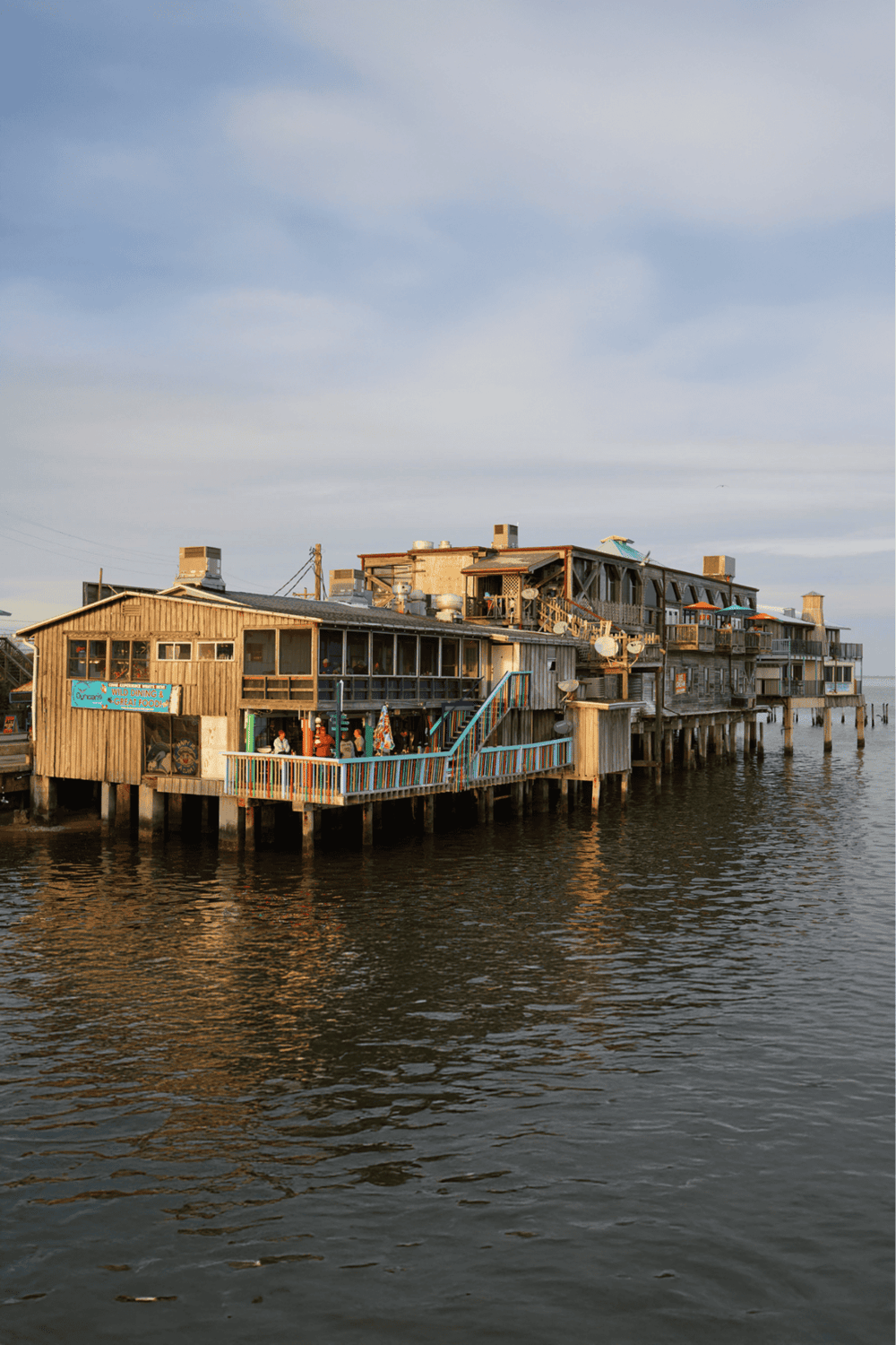 Colorful waterfront seafood restaurant on stilts with ocean view.