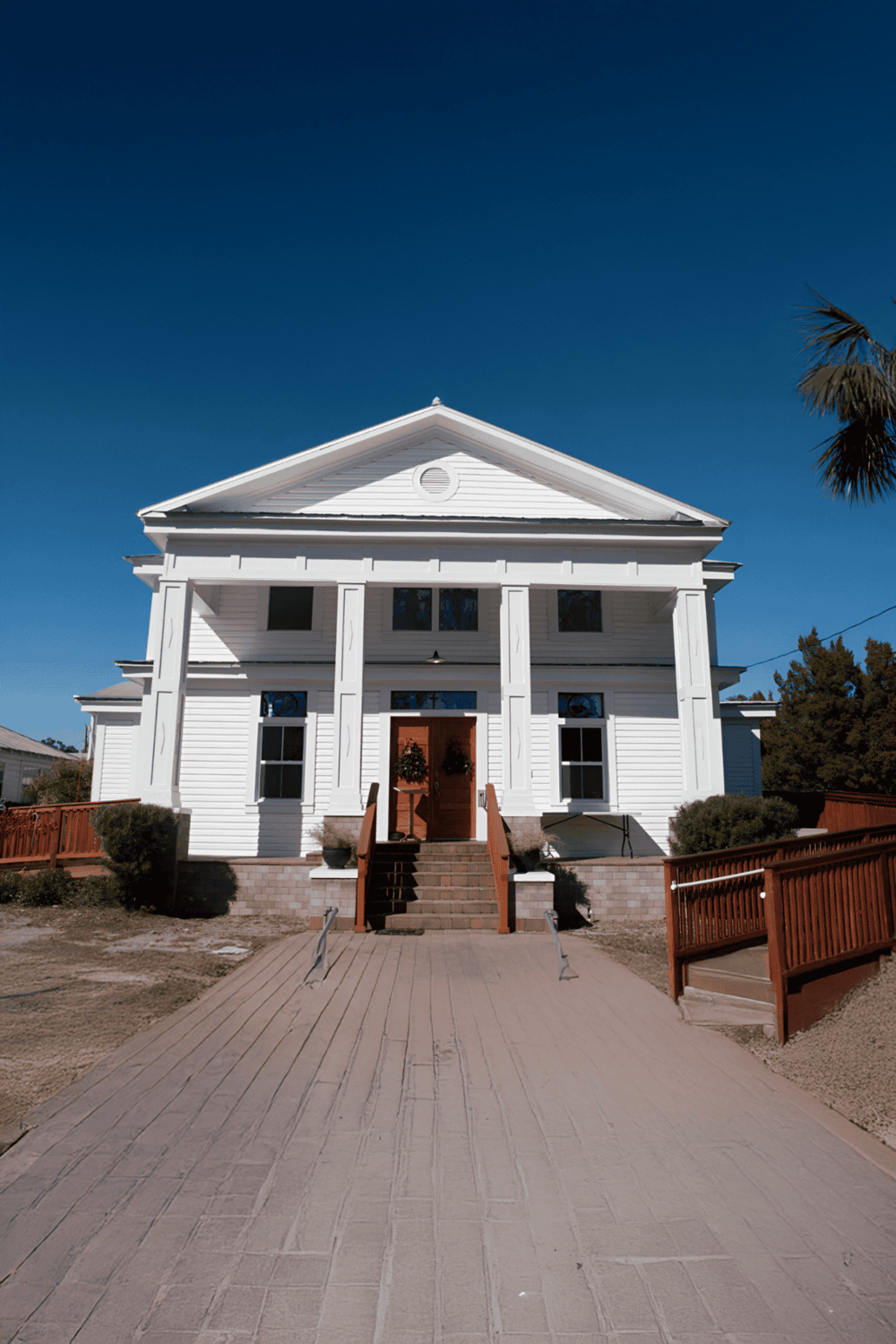 White restored house with steps, porch, and railings against clear blue sky.