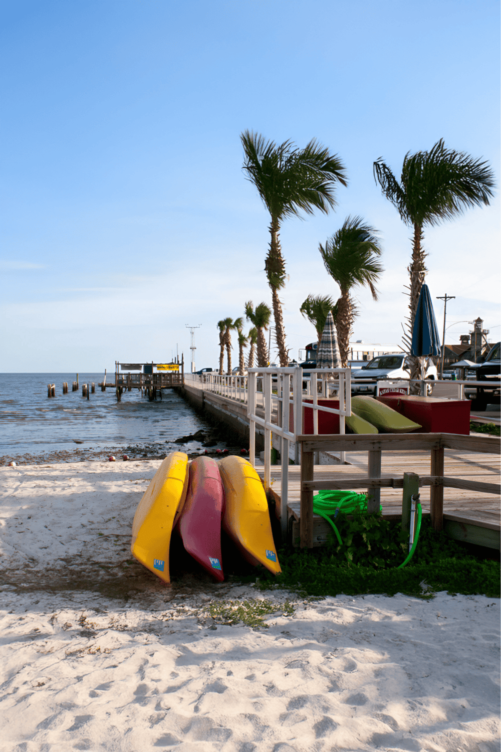 Colorful kayaks on beach near pier with palm trees and ocean view, popular Florida tourist destination.
