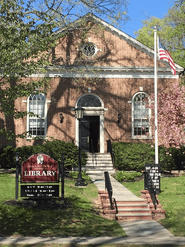 Bright red brick library building with American flag and blossoming trees in front.