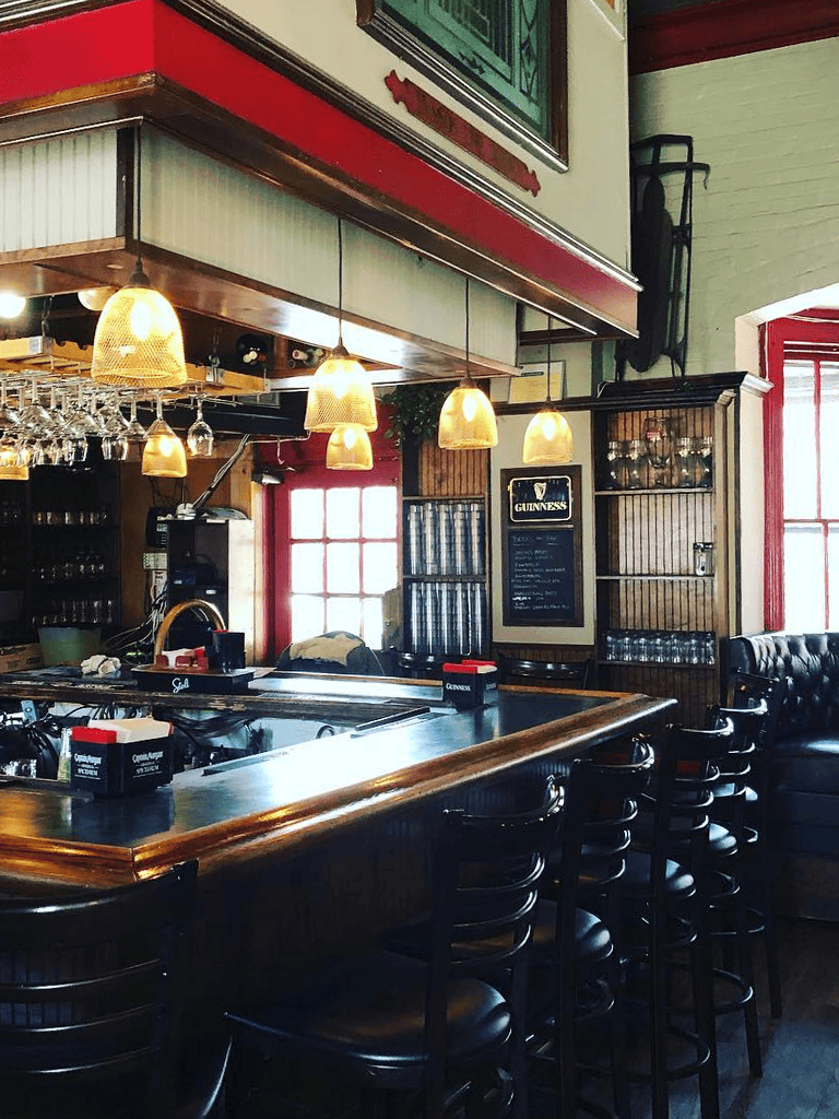 Cozy Irish pub interior at QuestForDirections restaurant with wooden bar, hanging lamps, Guinness chalkboard, and leather seating.
