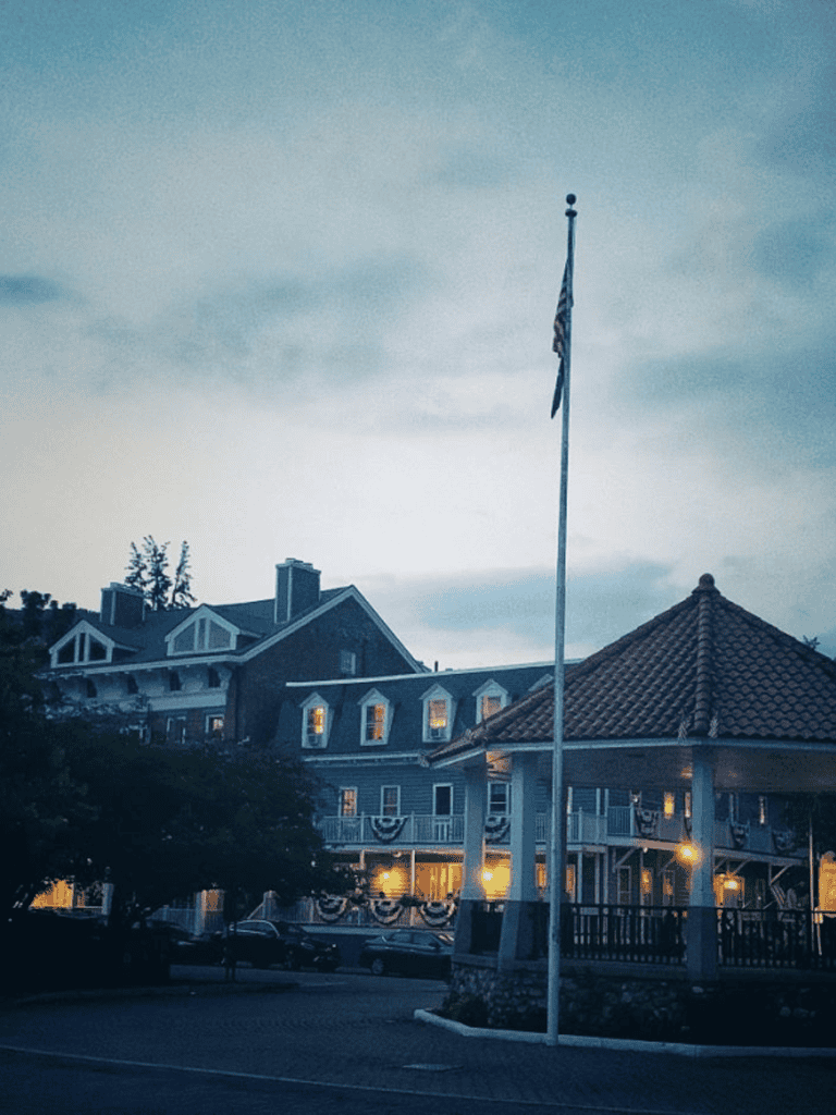 Flagpole with American flag in front of a large, charming hotel with classic architecture and warmly lit windows.
