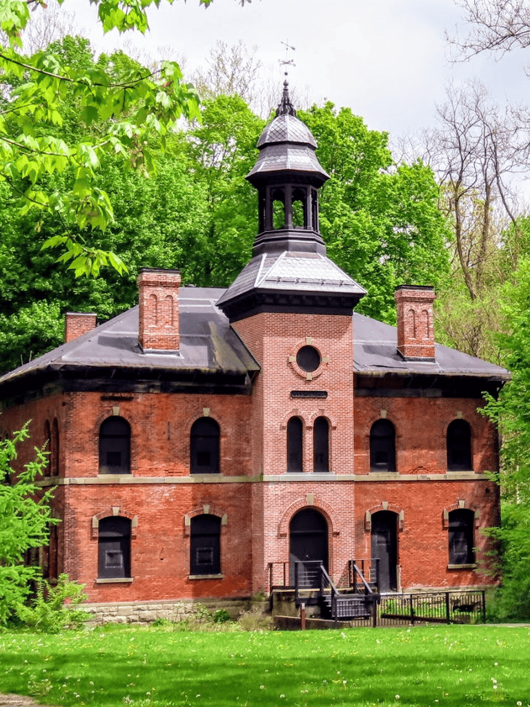 Historic brick building with a tower surrounded by lush greenery and trees.