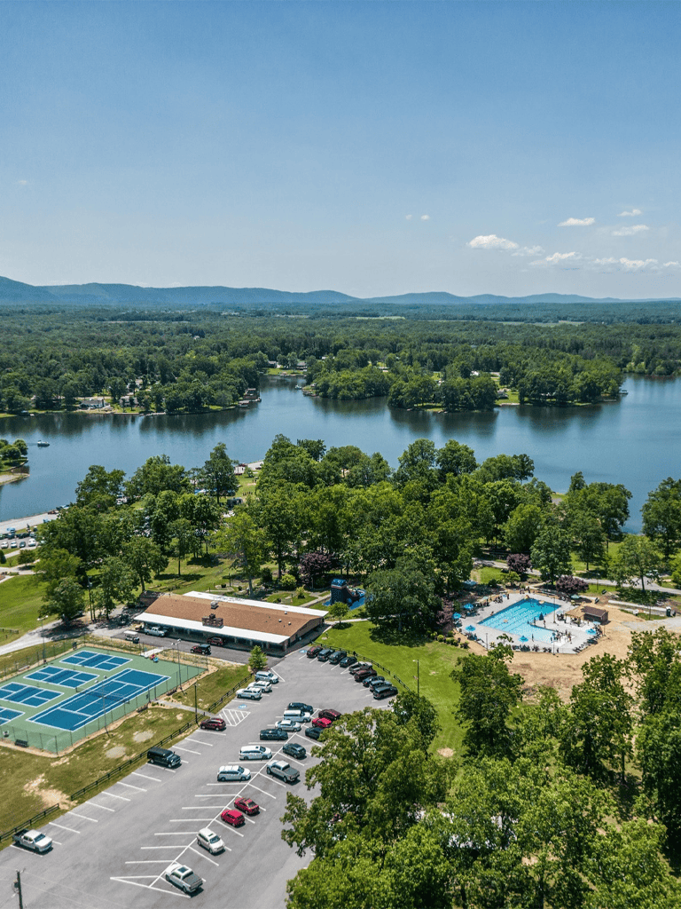 Serene lakeside recreation area with swimming pools, tennis courts, and parking, surrounded by lush greenery.