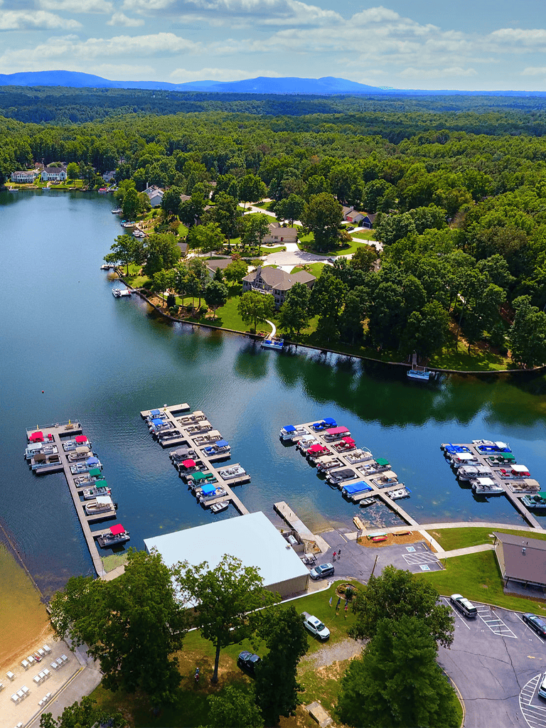 Boating marina with docks on a scenic lake surrounded by lush greenery and houses.