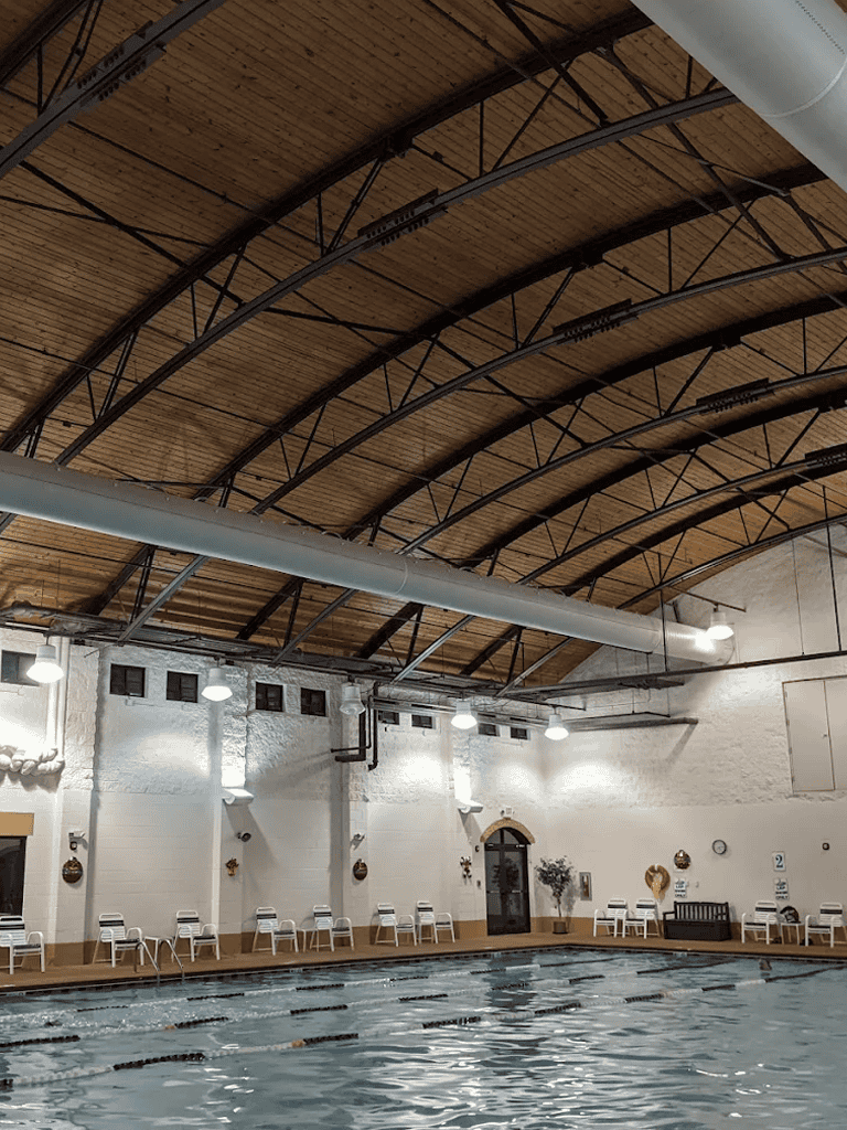Indoor swimming pool with wooden arched ceiling and white walls, ideal for fitness and leisure activities.