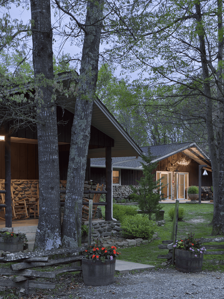Cozy rustic cabin surrounded by trees and flower pots, perfect for outdoor retreats.