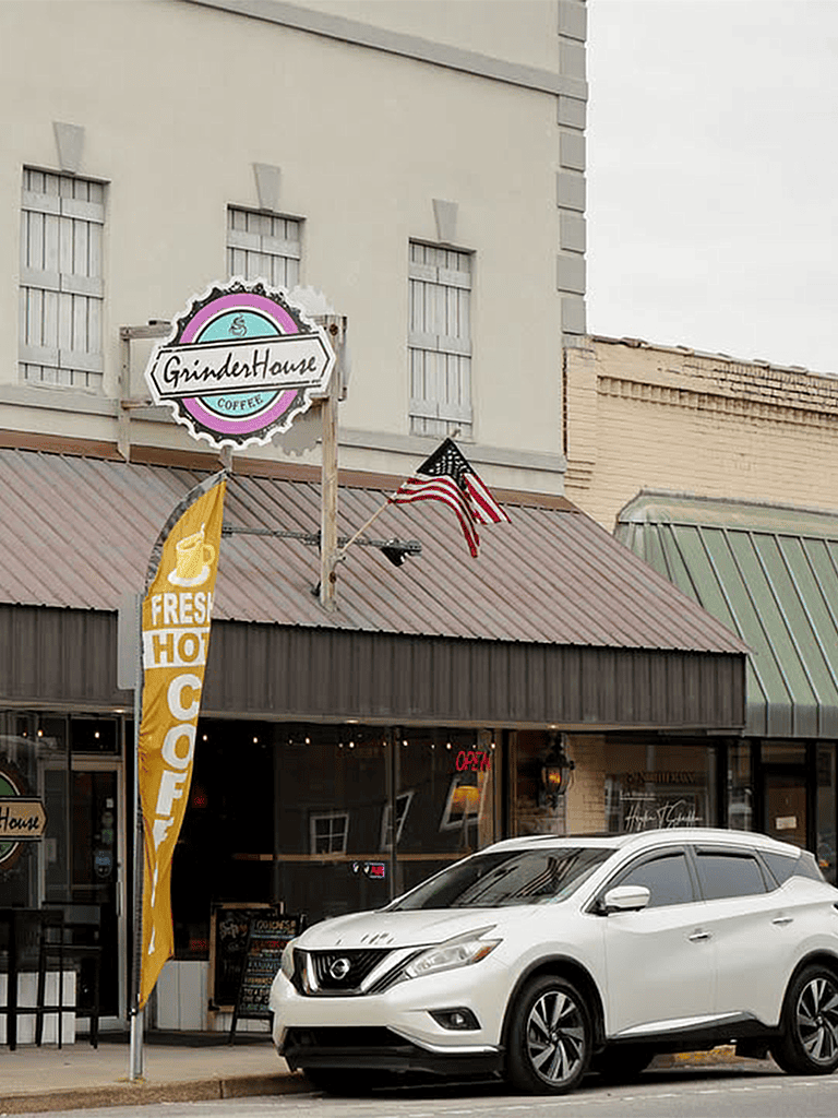 Coffee shop storefront with American flag, outdoor seating, and "GrinderHouse Coffee" sign.