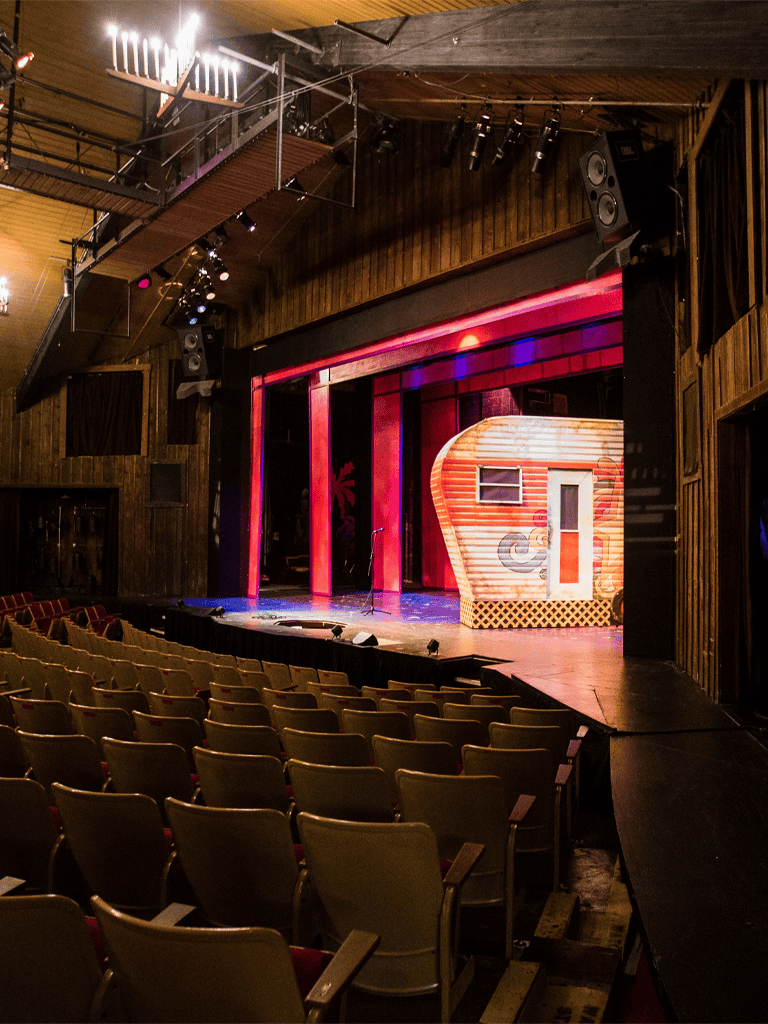 Open-air theater stage with colorful backdrop in a cozy, wood-paneled auditorium.