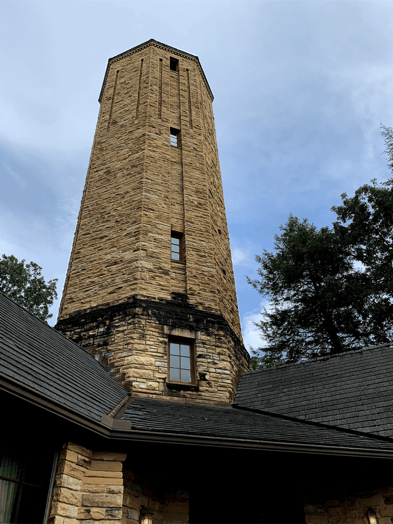 Old stone observation tower overlooking lush trees under a cloudy sky.