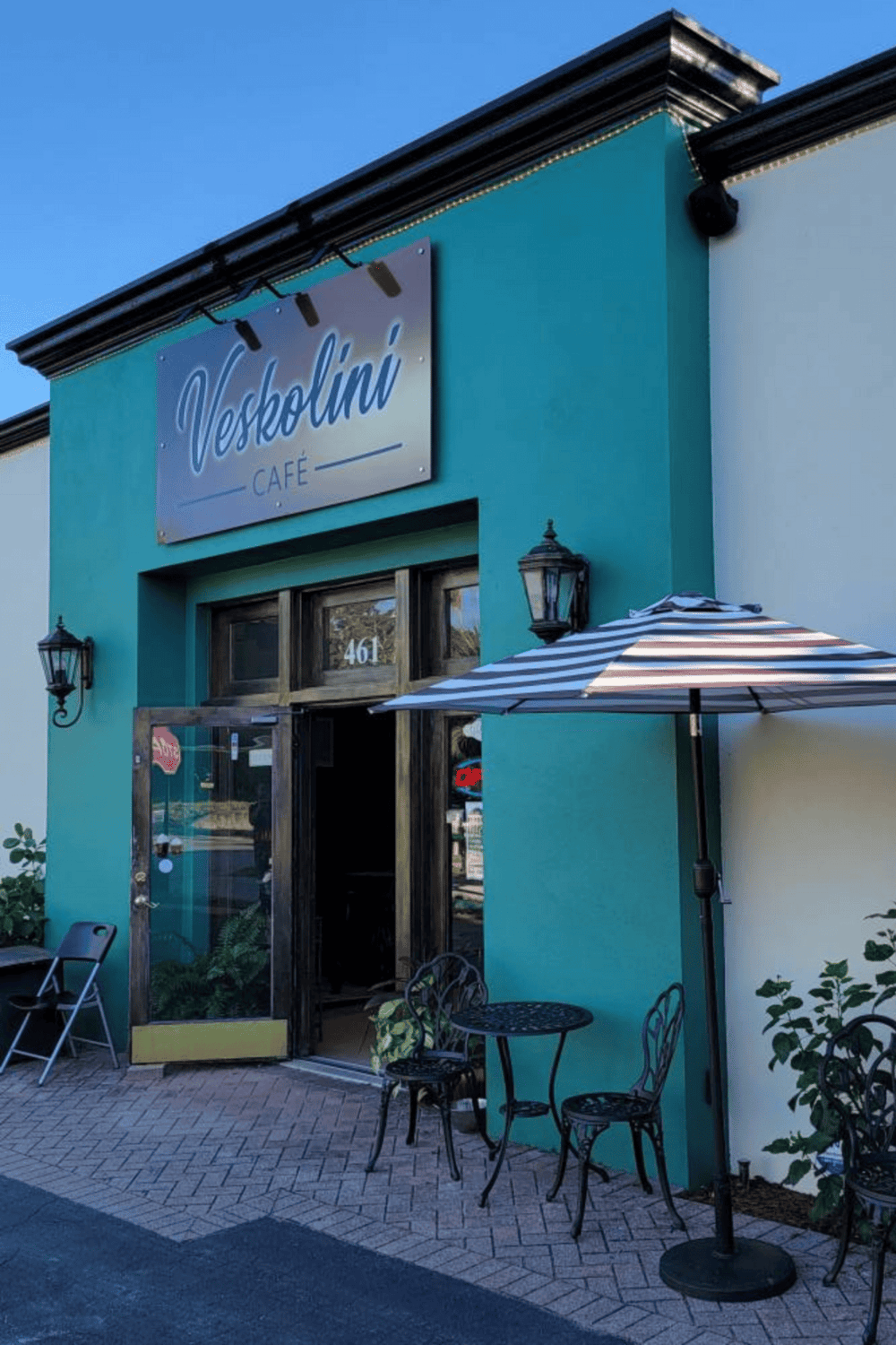 A vibrant teal coffee shop exterior with outdoor seating and a striped umbrella, inviting for local cafe visitors.