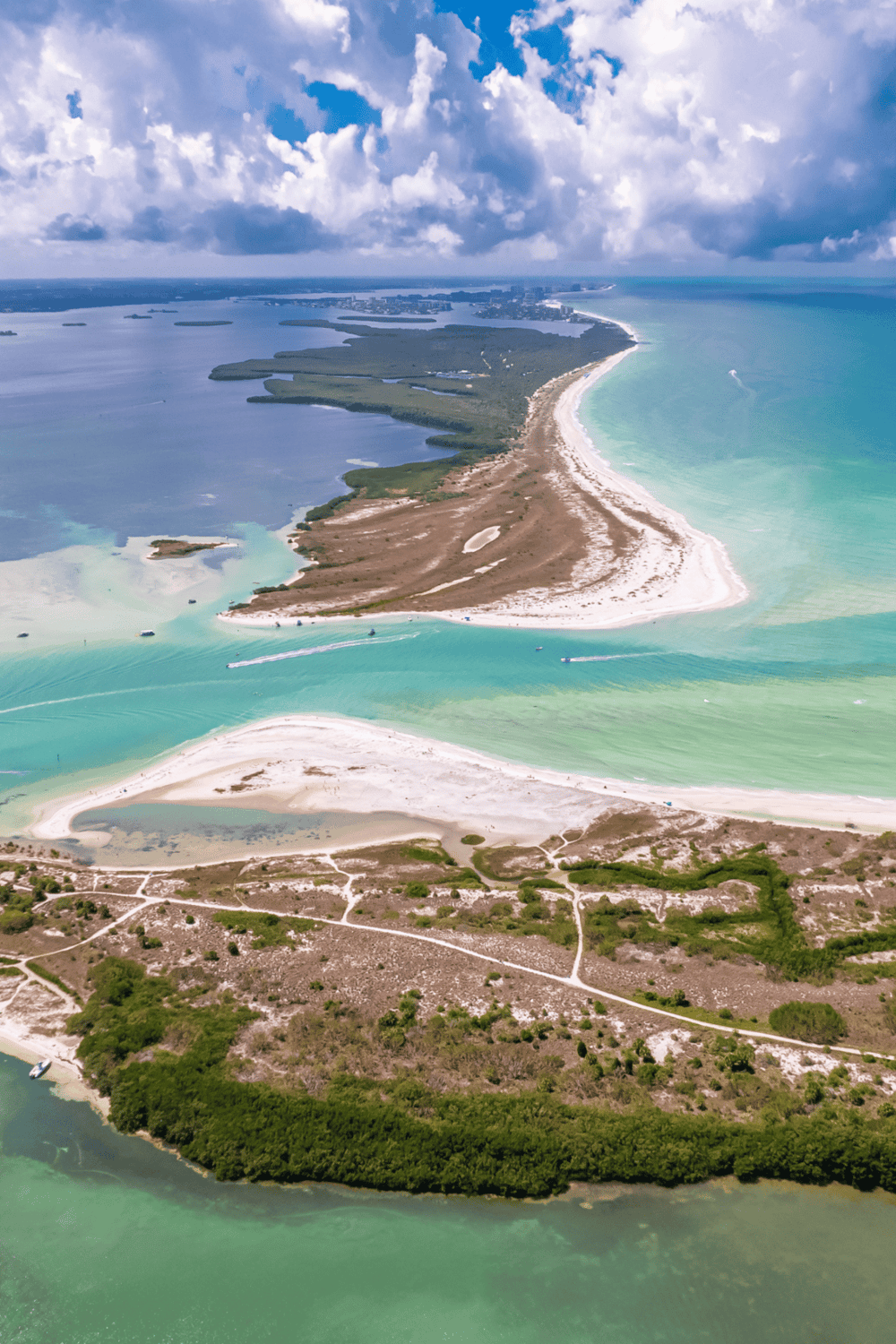 Aerial view of a barrier island with white sandy beaches, turquoise waters, and surrounding wetlands in Florida.