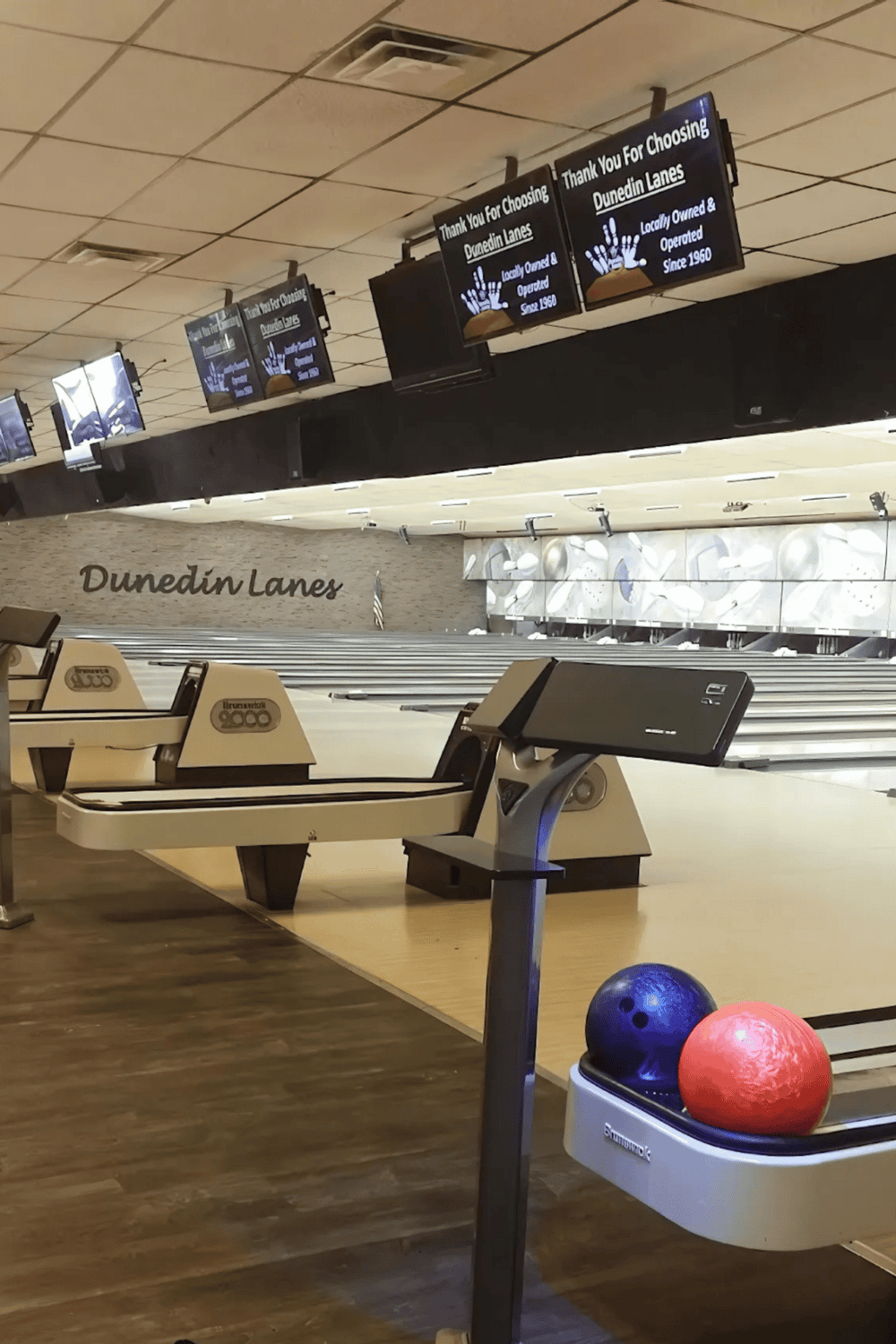 Empty Dunedin Lanes bowling alley, modern digital score screens, and colorful bowling balls for fun and entertainment.