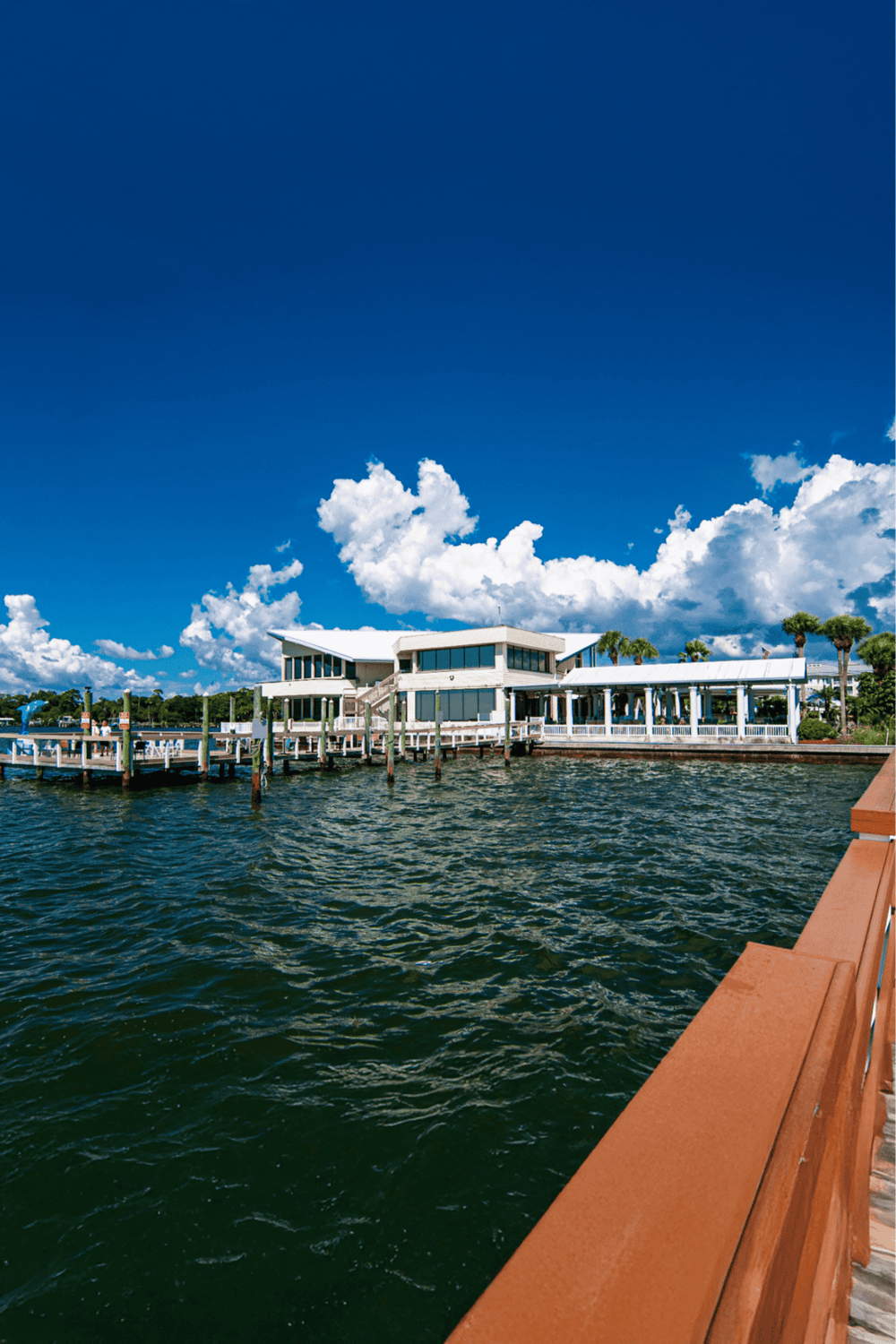 Waterfront building on a pier with blue sky and fluffy clouds, scenic location, perfect for travel and destination photography.