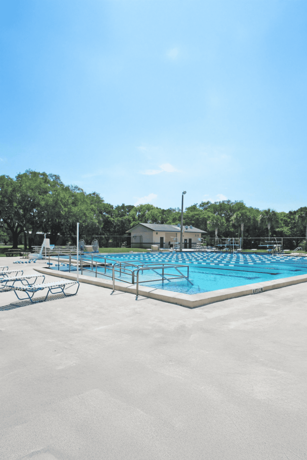 Clean outdoor swimming pool at QuestForDirections community with lounge chairs and lush trees in the background.