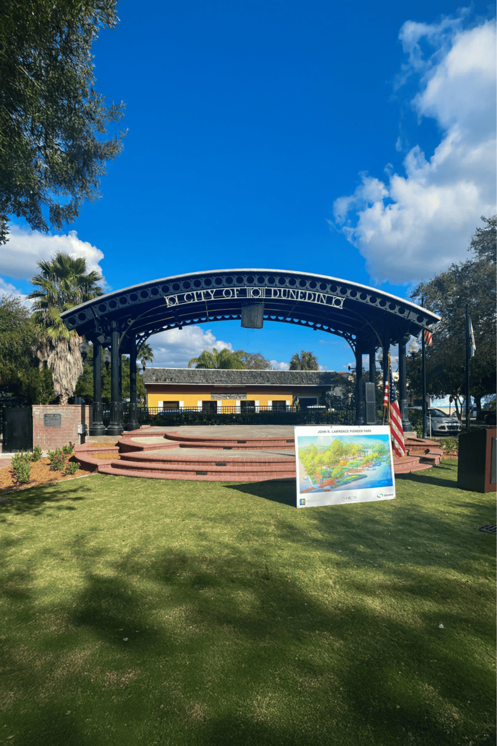 Historic downtown park with city engraving, lush greenery, and vibrant blue sky.