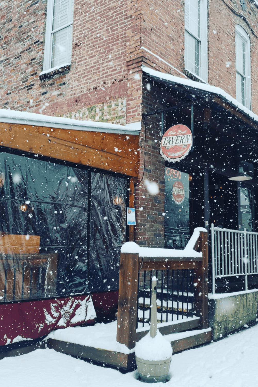 Cozy tavern entrance in snow, brick building, rustic wood accents, inviting atmosphere, winter scene, QuestForDirections.