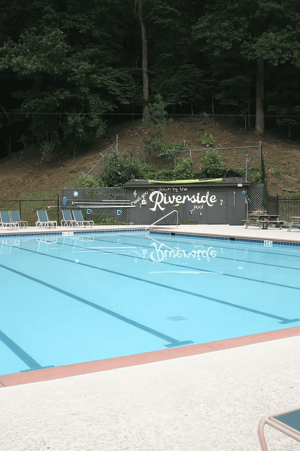Empty swimming pool at Riverside with relaxing outdoor setting and vibrant greenery nearby.