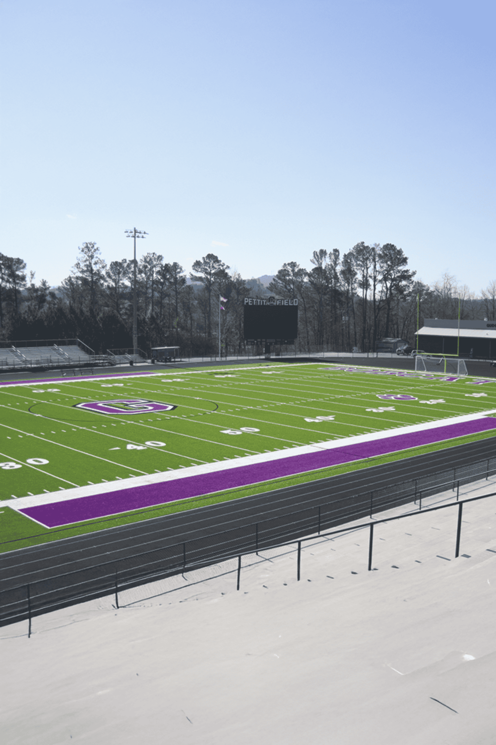 Bright green and purple football field at Pettiog State University with surrounding track and daytime sky.