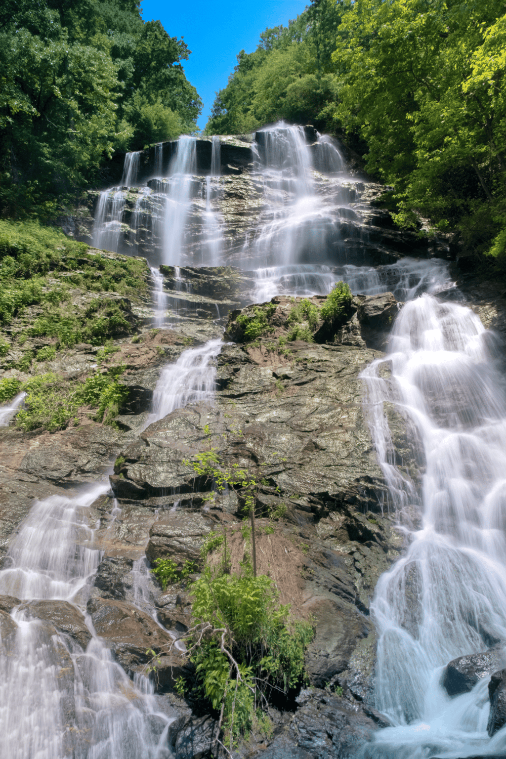 Waterfall cascading over rocky cliffs in lush green forest, scenic outdoor nature landscape.