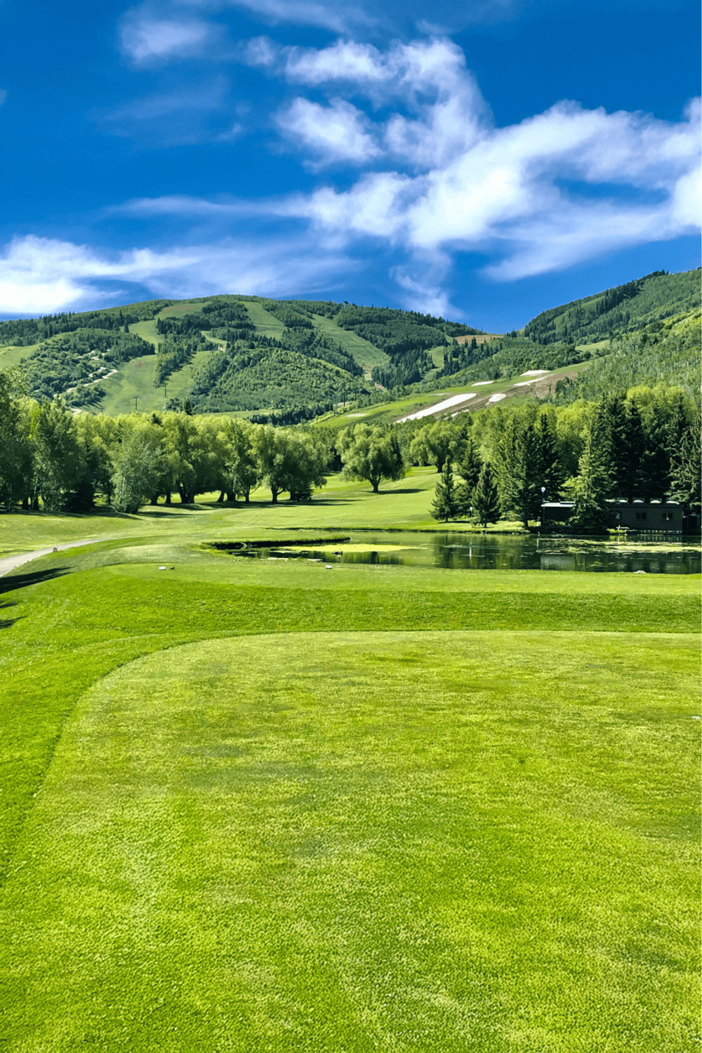 Lush green golf course surrounded by mountains and clear blue sky, perfect for outdoor recreation and golf adventures.