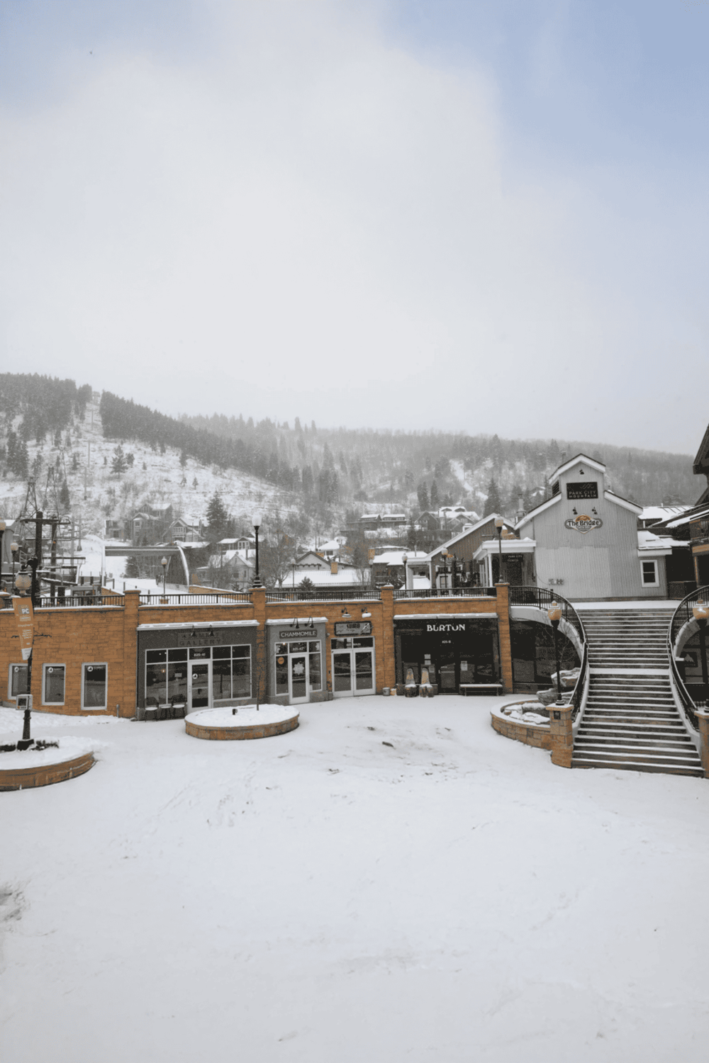 Snow-covered shopping area in a mountain town with ski slopes in the background.