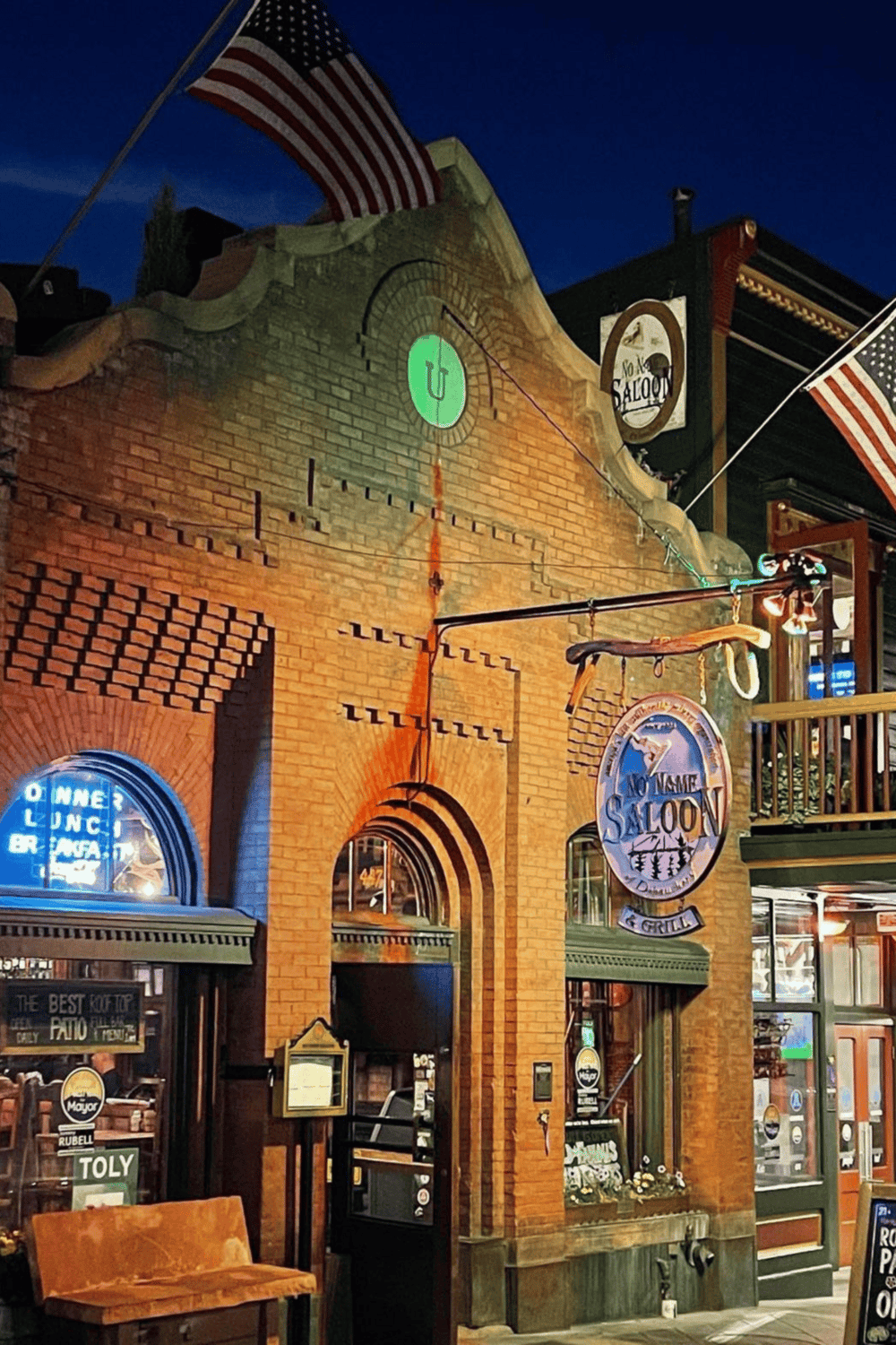 Warm neon-lit downtown bar with historic brick facade and American flags, perfect for casual dining and nightlife.