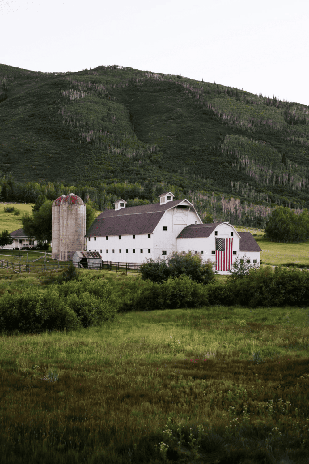 Rustic white barn with American flag, surrounded by lush green fields and rolling hills.