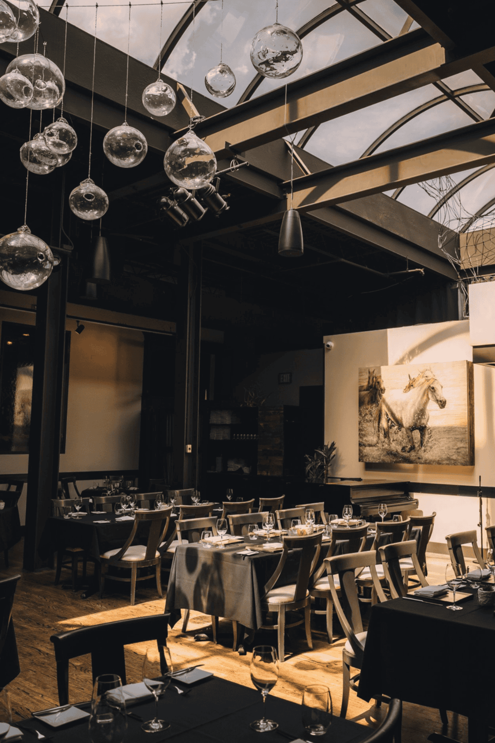 Elegant restaurant interior with hanging glass globes and framed horse artwork, ideal for fine dining and events.