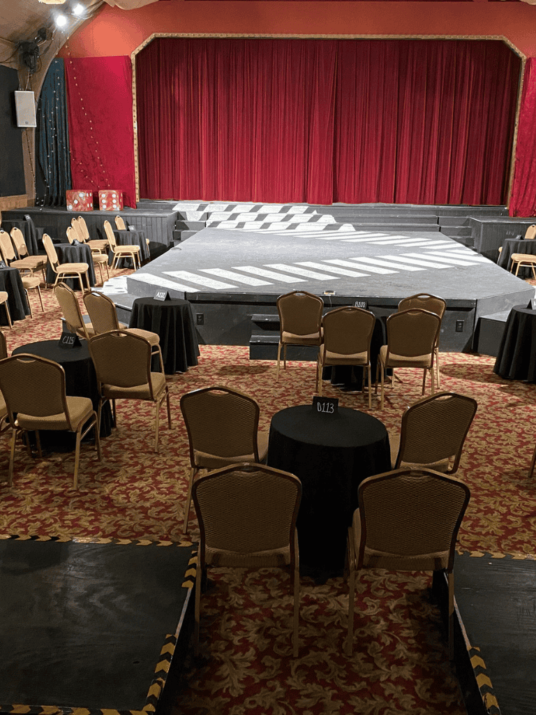 Indoor event stage with seating arrangement and red curtain backdrop at QuestForDirections venue.
