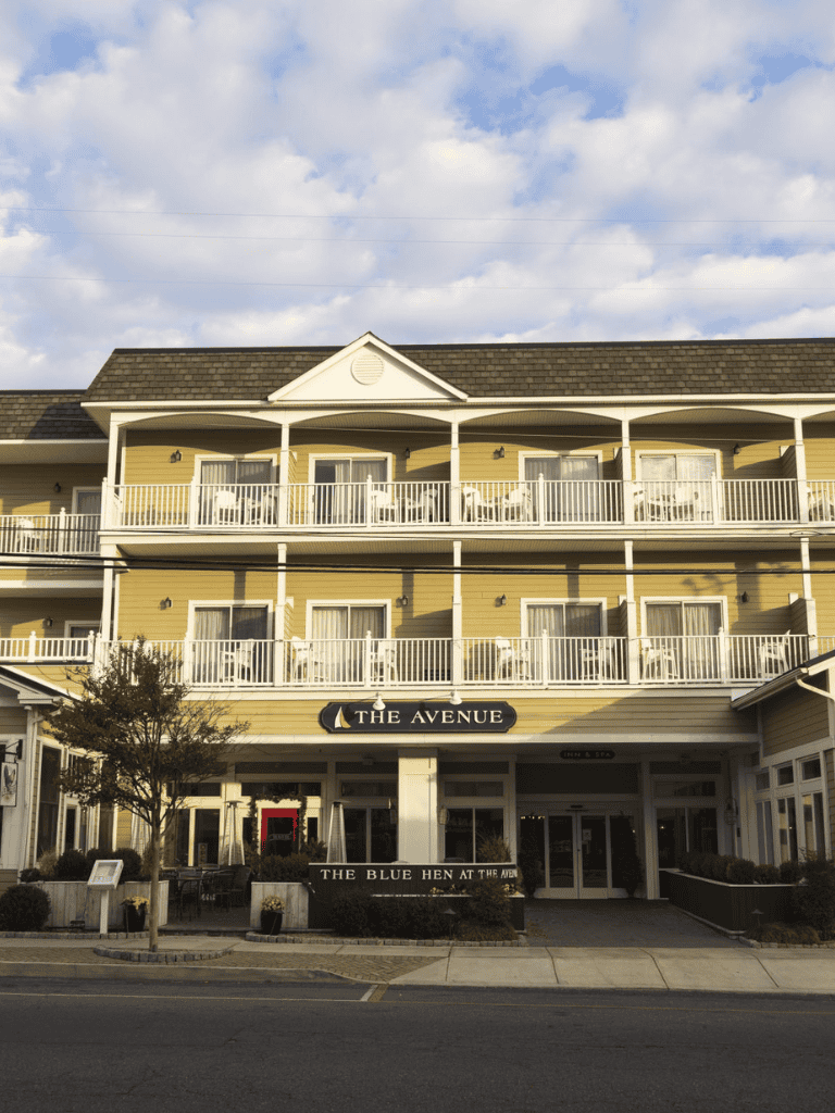 Charming seaside hotel with balconies, outdoor seating, and clear blue sky.