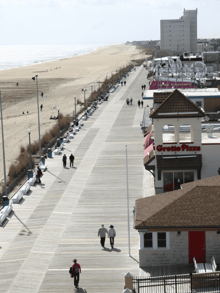 Seaside boardwalk with benches, cafes, and ocean view, vibrant beach destination, scenic coastal walk in summer.