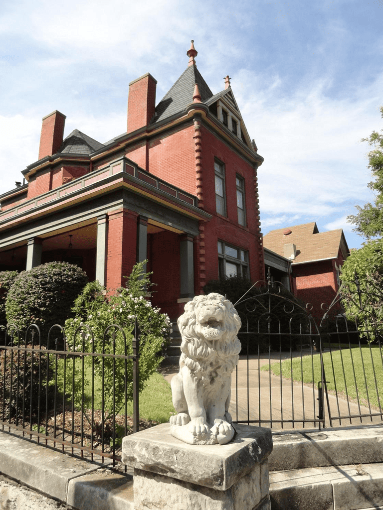 Elegant Victorian style red brick house with lion statue in front yard, historic home exterior, architecturally detailed residential building.