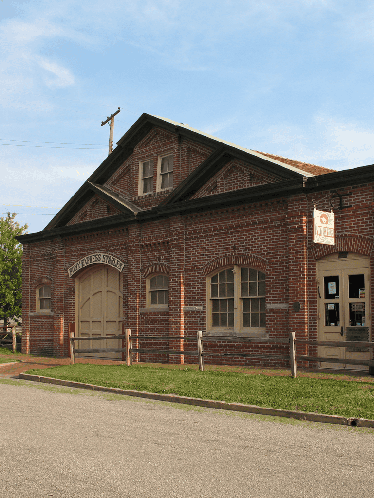 Old brick building with Ponca Express Stables sign, historic rural setting, blue sky, inline parking, vintage architecture.