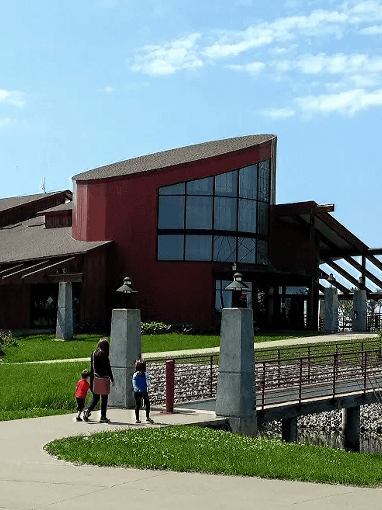 Modern building with large glass windows, family walking on a curved sidewalk, bright sunny day, QuestForDirections.