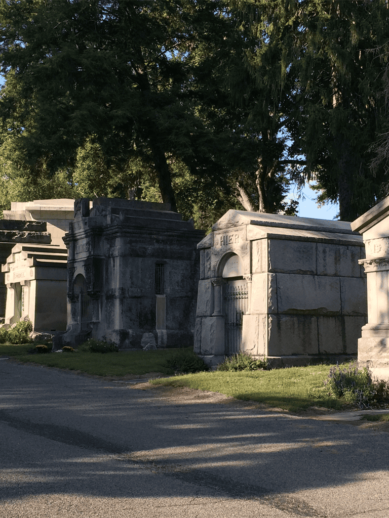 Ancient tombstones and mausoleums in a historic cemetery featuring stone architecture and lush greenery.