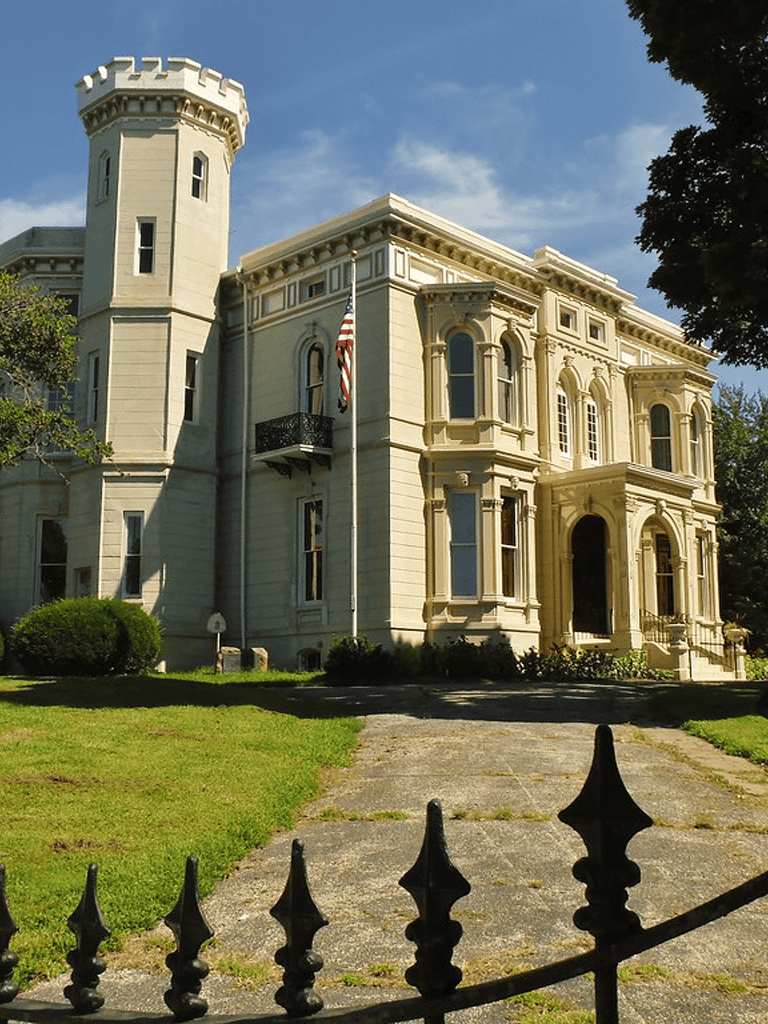 Elegant historic castle-style mansion with castle turret and lush greenery.