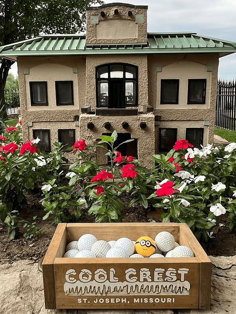 Miniature house sculpture at Cool Crest, St. Joseph, Missouri with flower beds and a golf-themed box of golf balls.