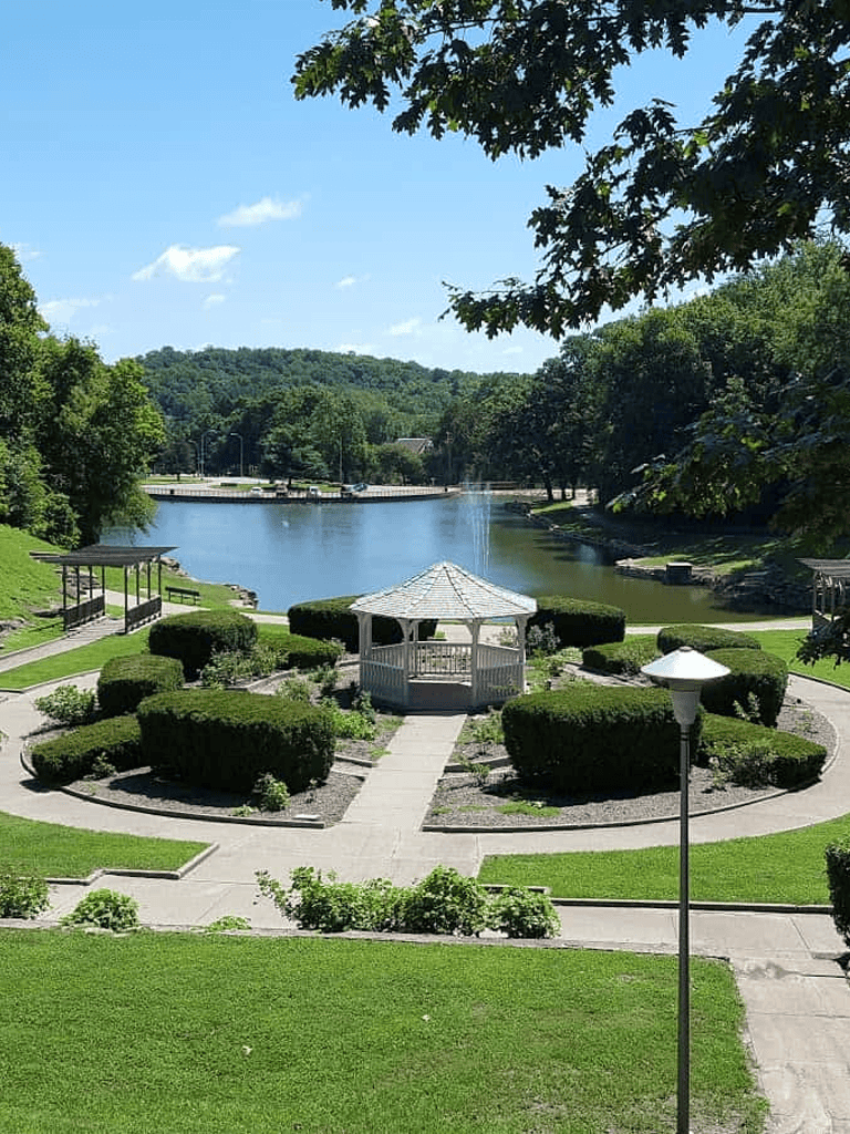 Serene park with a gazebo by a lake, lush greenery, and outdoor seating, perfect for relaxation and outdoor activities.