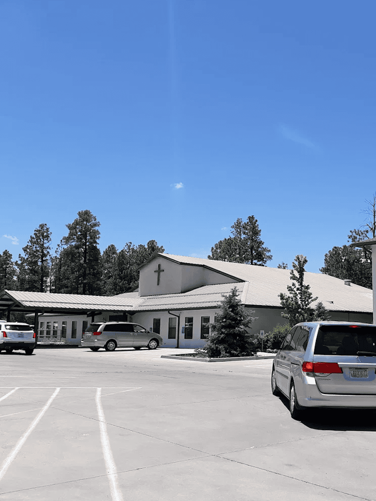 Quiet church with parking lot and pine trees on a sunny day.