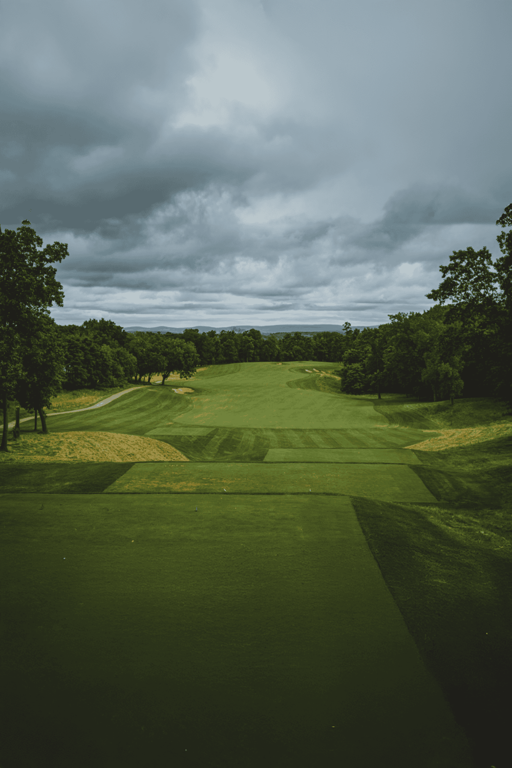 Golf course under cloudy sky with lush green trees and rolling fairways.