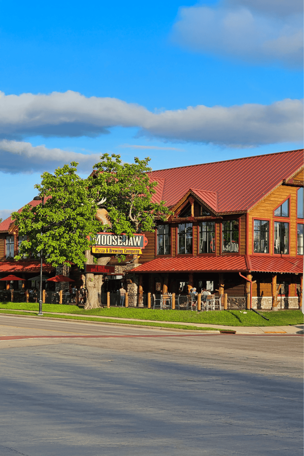 Relaxed restaurant exterior with red roof and green trees in front, inviting dining experience at Moosejaw Pizza & Brewing.