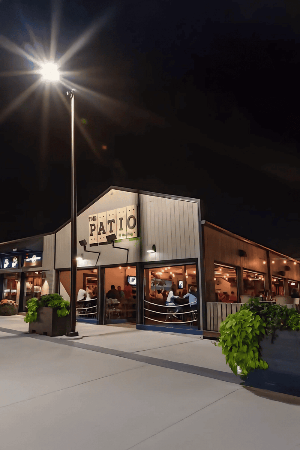 1. Modern restaurant patio outdoor dining at night with warm lighting and greenery.