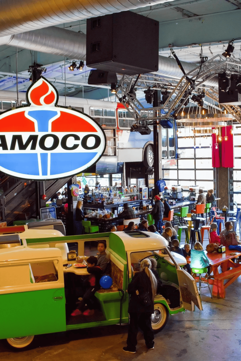 Amoco gas station sign inside a vibrant shopping arcade with retro decor and diverse visitors.