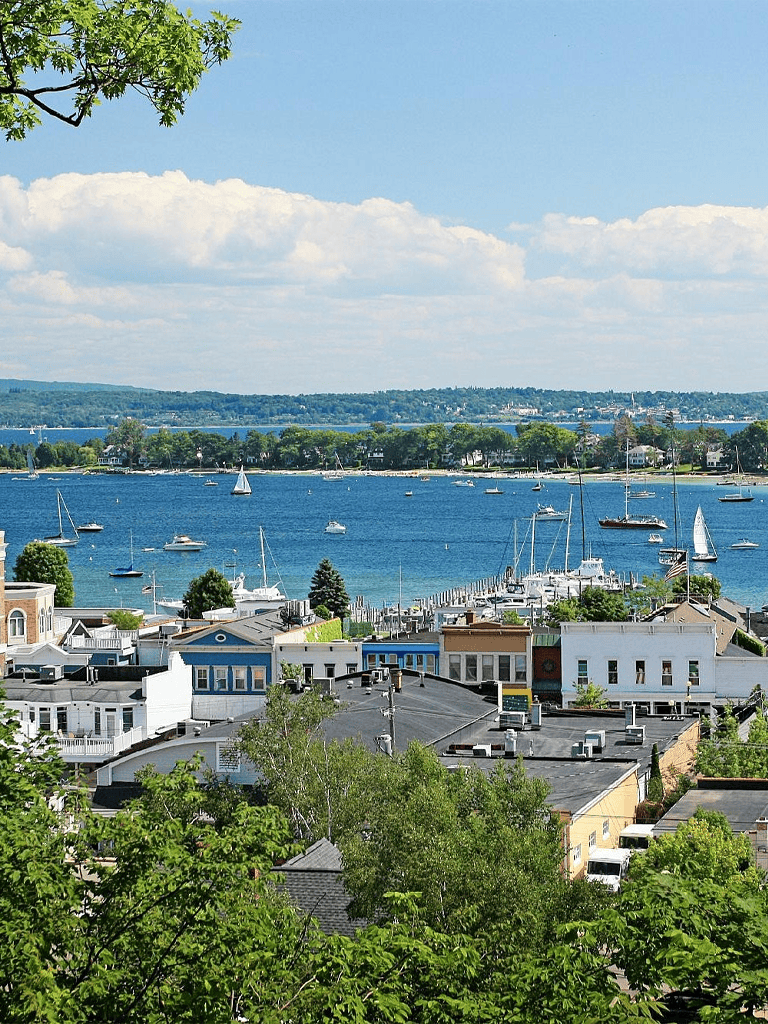 Colorful waterfront town with sailboats on a calm bay under a partly cloudy sky.